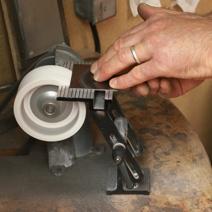 Then grind the bevel. Unlike a card scraper, whose edges are square to its faces, the cabinet scraper blade gets a 45° bevel along its cutting edge. The bevel can be straight across or slightly cambered. And you can file the bevel instead of grinding it if you choose.