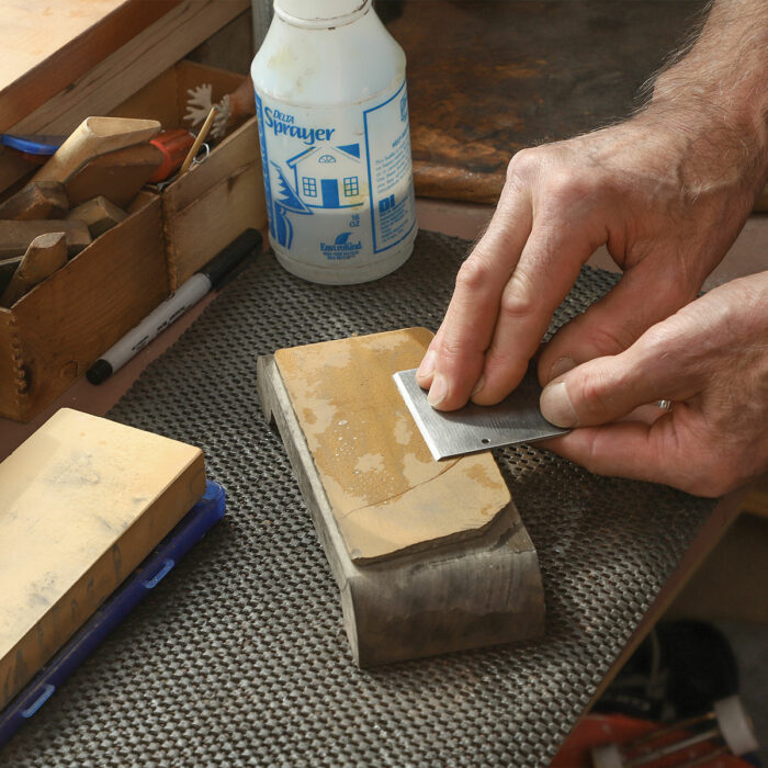 Flatten the back first. Just as he would with a plane blade, Coleman hones the flat side of the scraper blade to obtain a mirror finish behind the bevel.